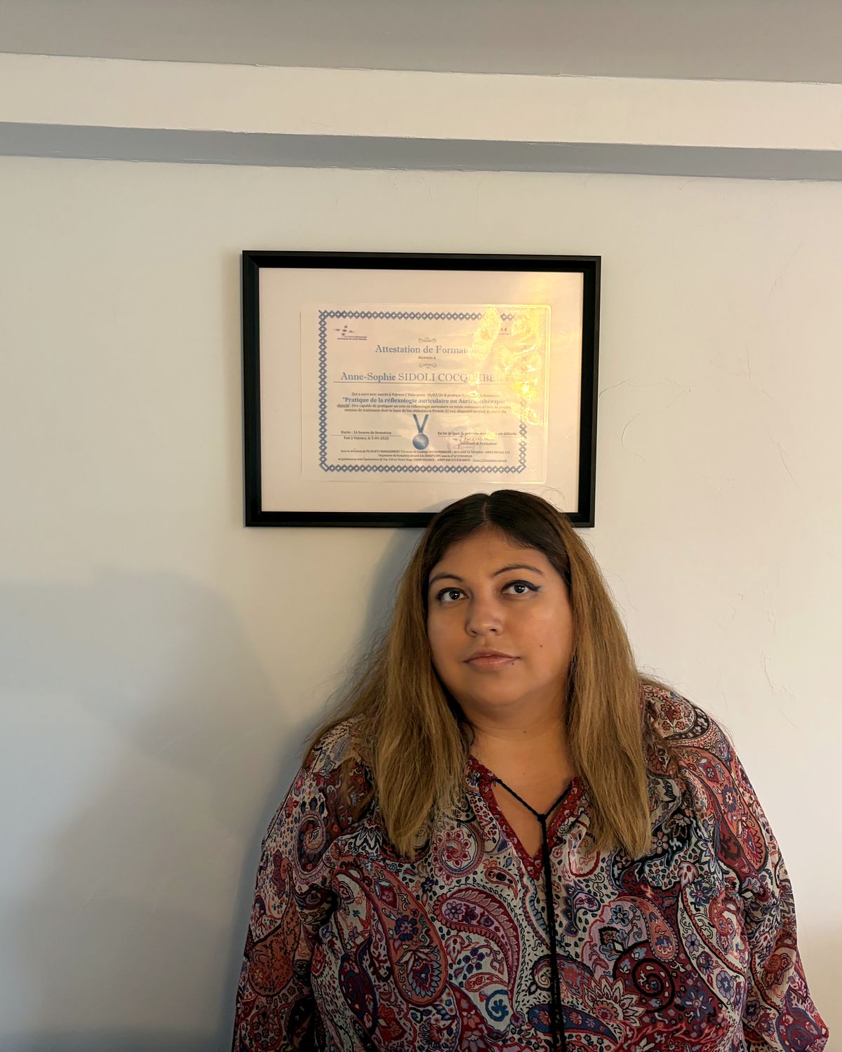 Anne-Sophie SIDOLI dans son cabinet d’Amfreville-la-Mi-Voie, devant son attestation de formation en réflexologie auriculaire encadrée